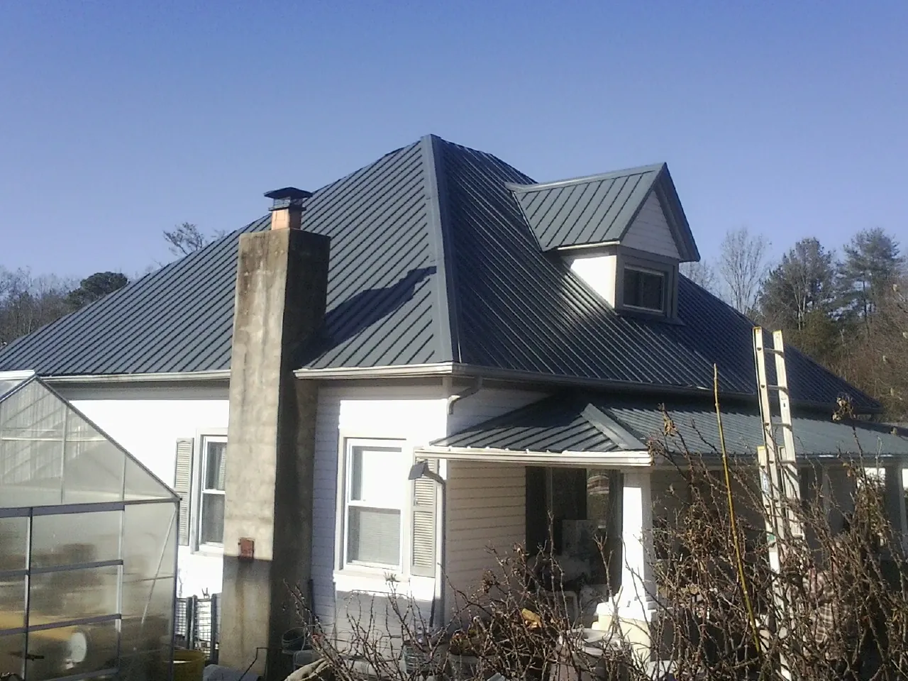 Dark blue standing seam metal roof on a white farmhouse with dormer — Slate & Tile Roof Repair by Roofing Brothers in Ravena