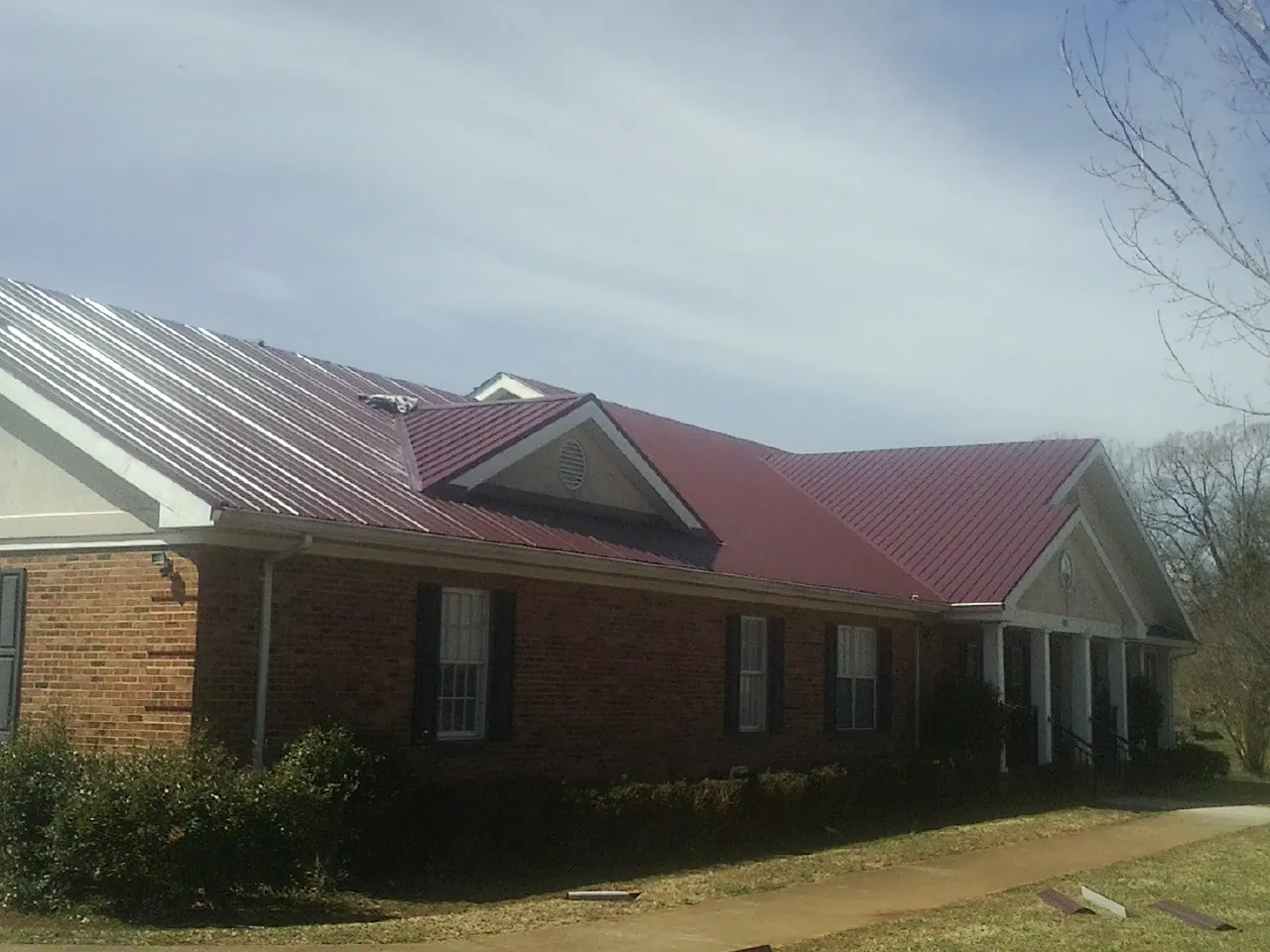 Red metal roof with gabled entries on a long brick building, from a Hail Damage Roof Repair job in Ravena