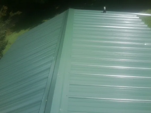 New green metal panels meeting at the ridge of a roof — Flat Roof Repair work by our crew in Ravena