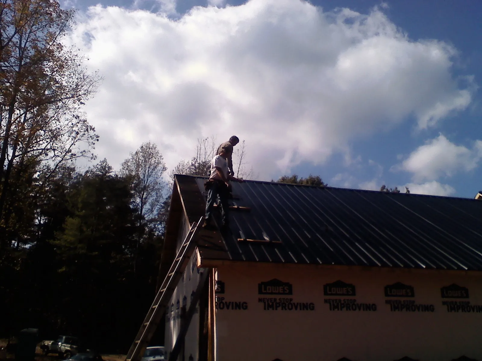 Roofer fastening dark metal panels high against a cloudy sky, from a Roof Inspection job in Ravena