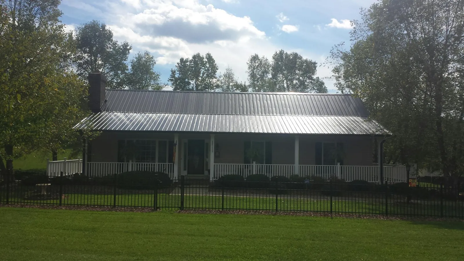 Gray metal roof on a brick ranch with a full width front porch — Gutter Guard Installation work by our crew in Ravena