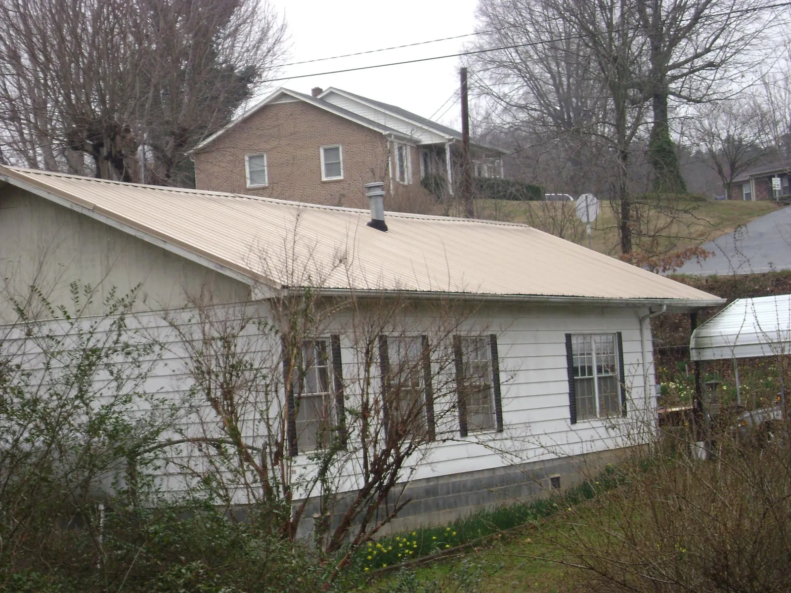 Tan metal roof on a white sided house set into a hillside — Commercial Roofing by Roofing Brothers in Ravena